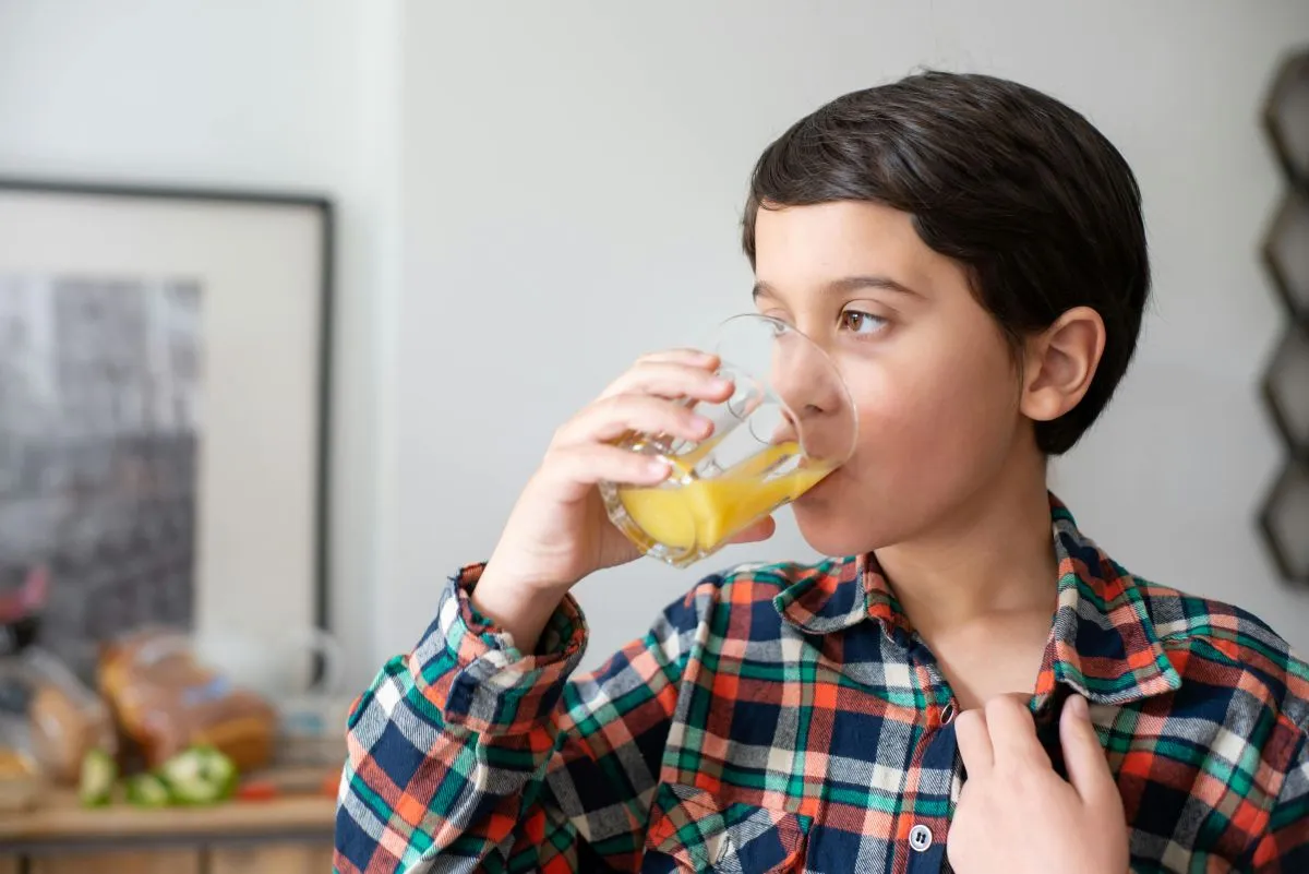 Un niño bebiendo un vaso de jugo, como parte de un hábito diario saludable que incluye el consumo de vitaminas para reforzar sus defensas de forma natural.